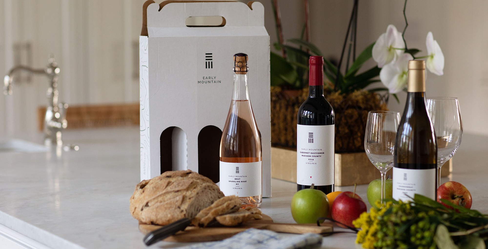 Early Mountain wine bottles on a counter with a wine box in the background and some food items in the foreground.
